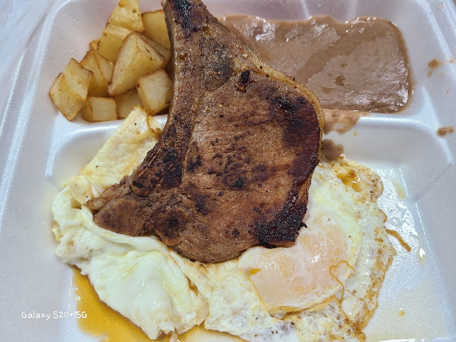 Pork chop breakfast plate with fried egg, potatoes and refried beans