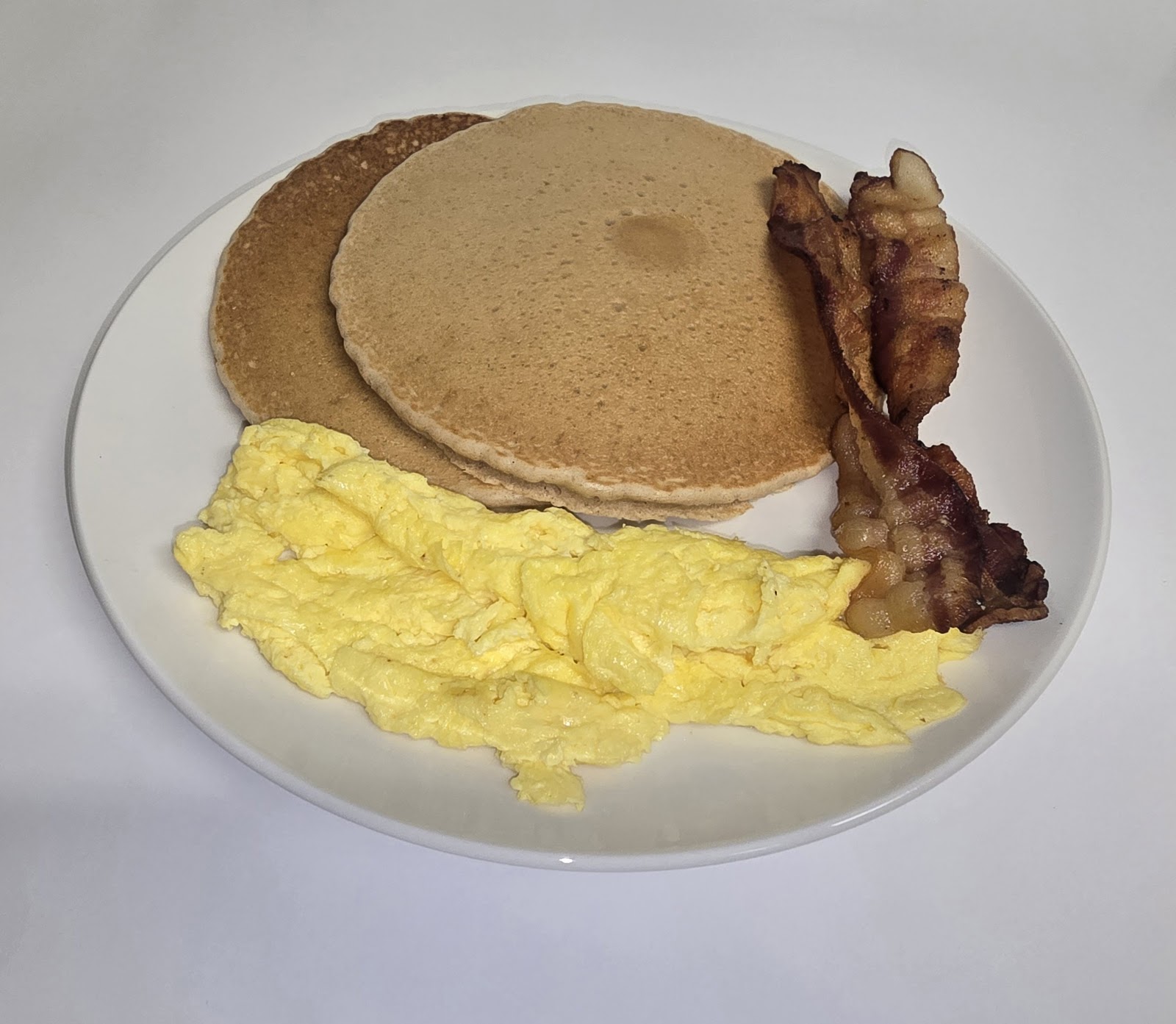 Pancakes with scrambled eggs and bacon breakfast plate